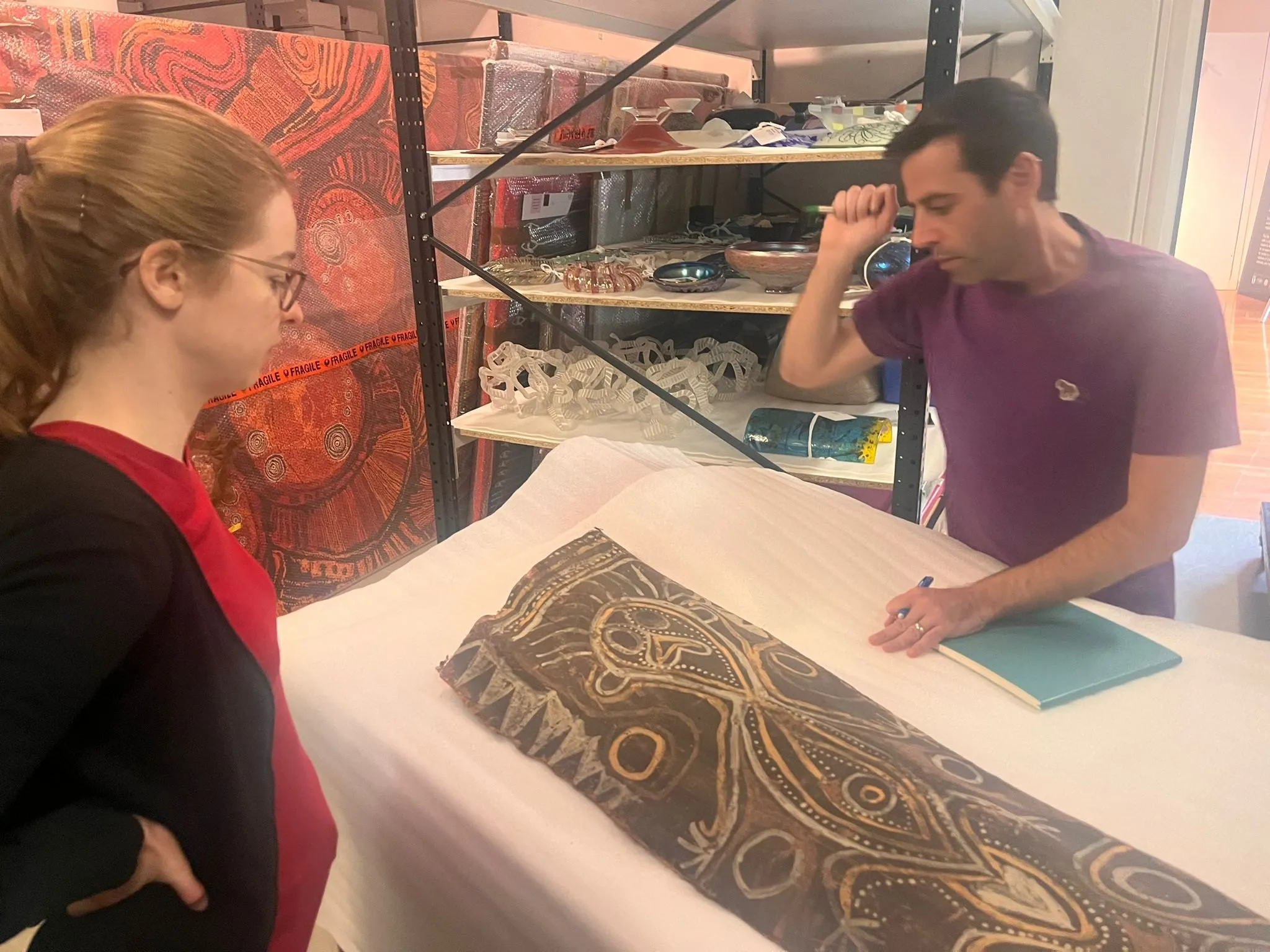 Three people lean over the sago palm spathe panel, laid flat on tissue paper on a table in the collection store