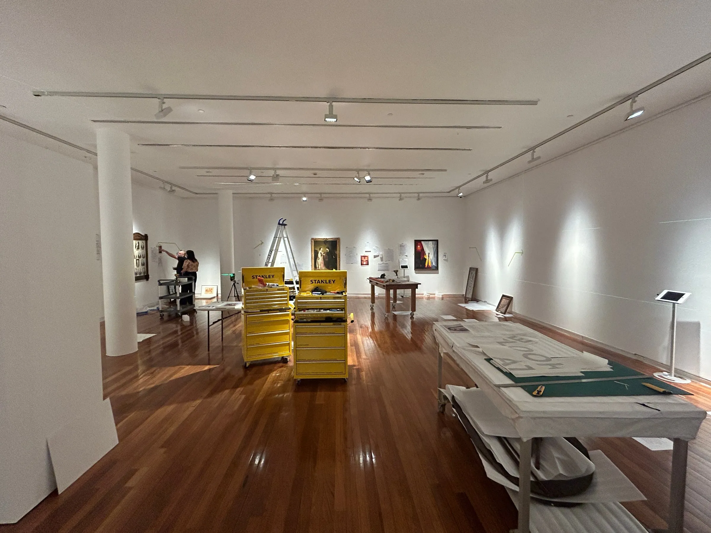 The empty gallery during installation, with crates, a table of materials and works leaning against the walls