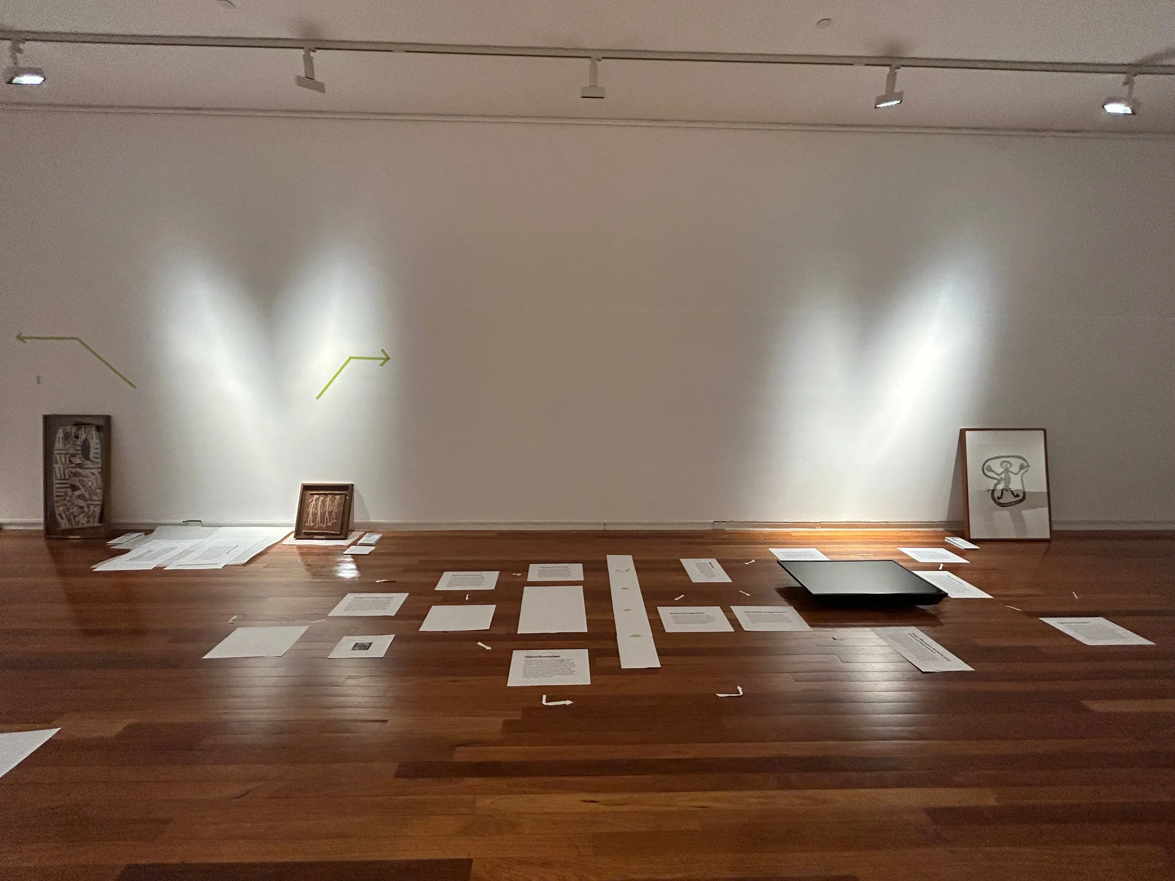 Printed wall texts laid out in rows on the gallery floor beneath the lights