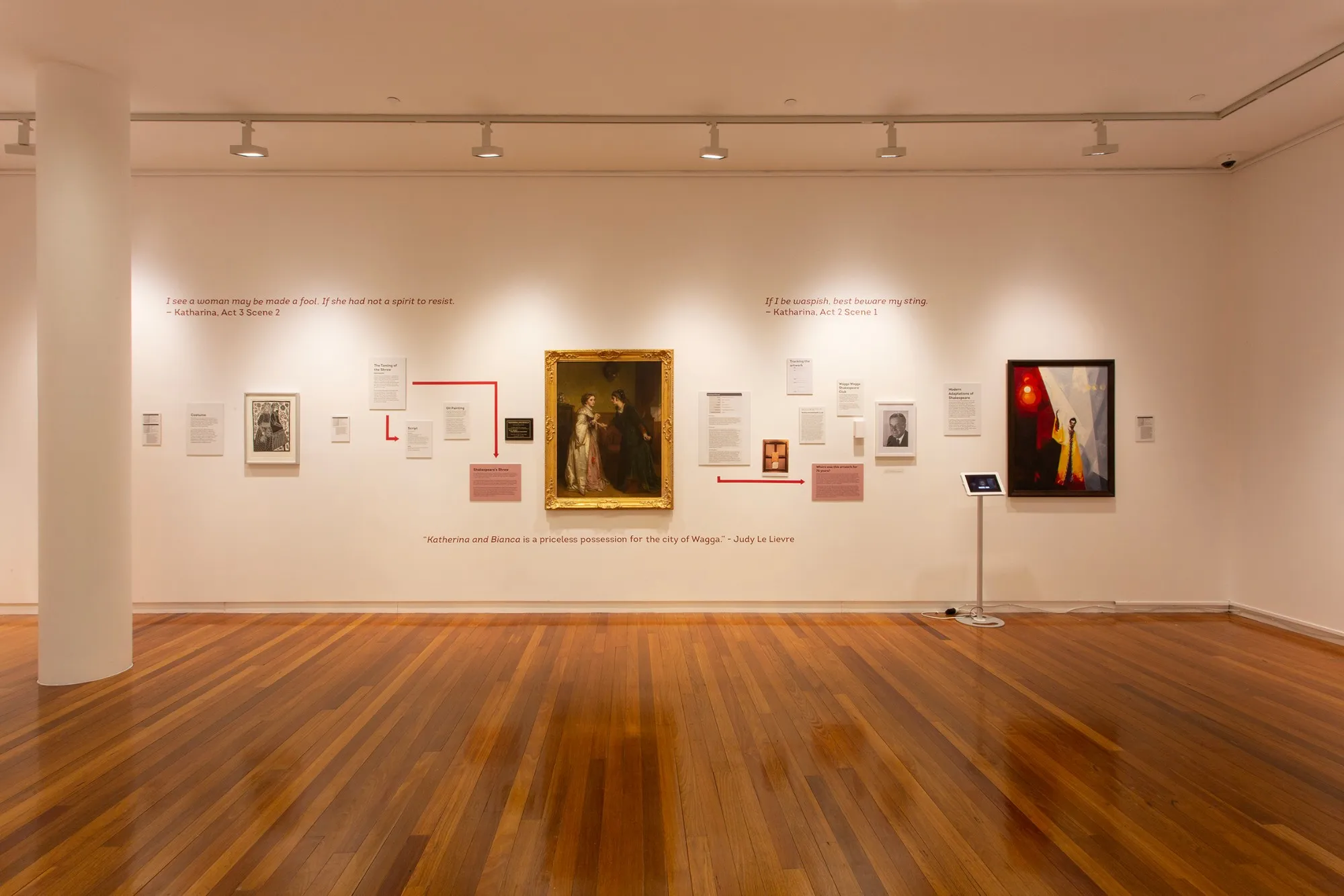 The red wall of Look at Me: Katherina and Bianca in its gilt frame at the centre, with wall texts joined by red arrows and quotations from The Taming of the Shrew above