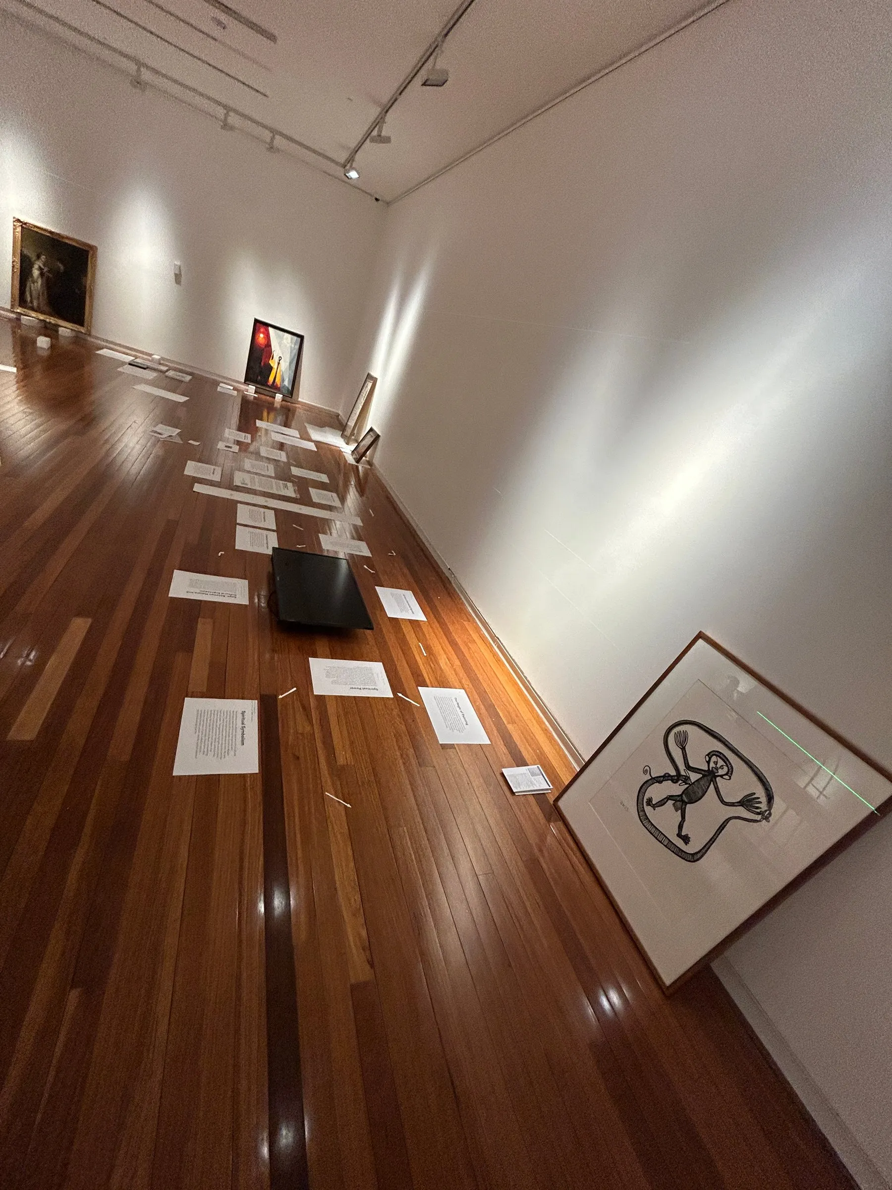 Works and labels laid out on the floor along the wall, waiting to be hung